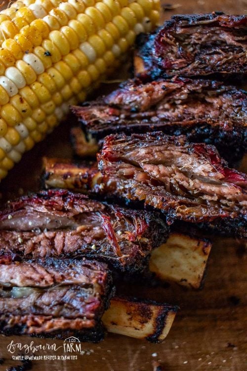 Close-up of smoked beef ribs paired with corn on a cutting board.