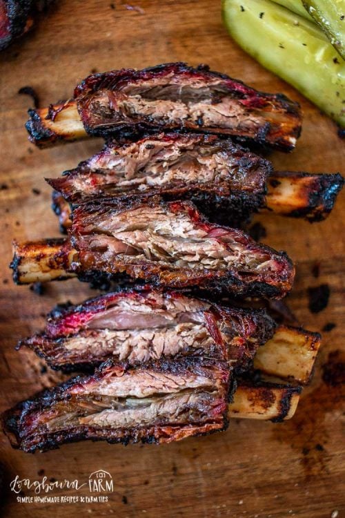 Smoked beef ribs lined up on a cutting board. 