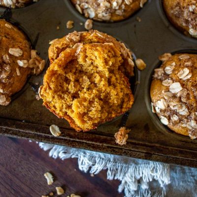 Pumpkin muffins in a muffin tin with one broken in half. Close-up.