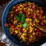 canned corn with bacon, red bell pepper and fresh herbs in a bowl with a spoon