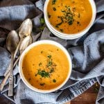Two bowls filled with creamy pumpkin soup, vertical.