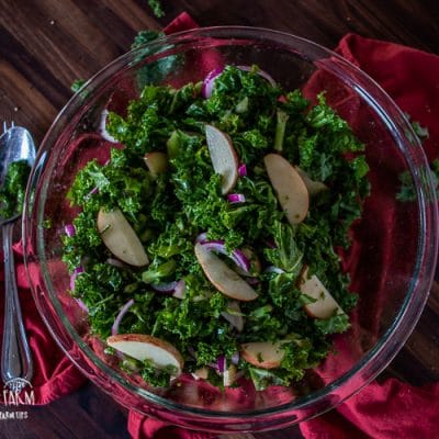 Kale apple salad in a bowl sitting on a red towel.