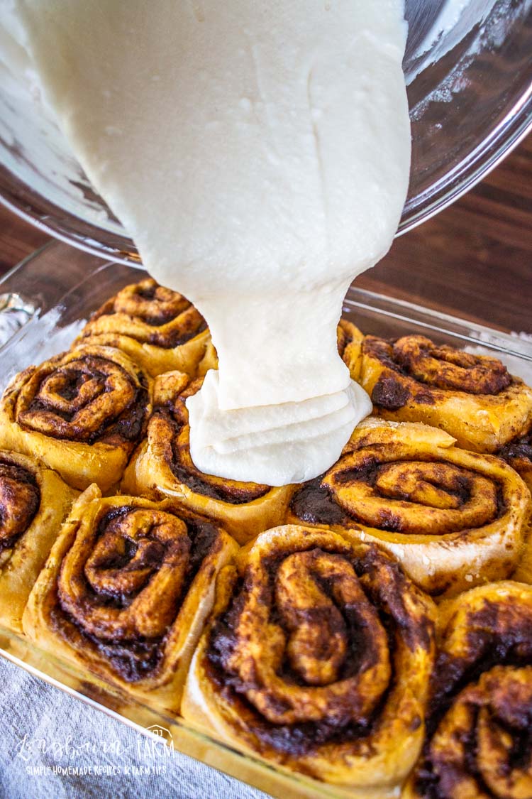 pouring the glaze over the tops of the baked pumpkin cinnamon rolls