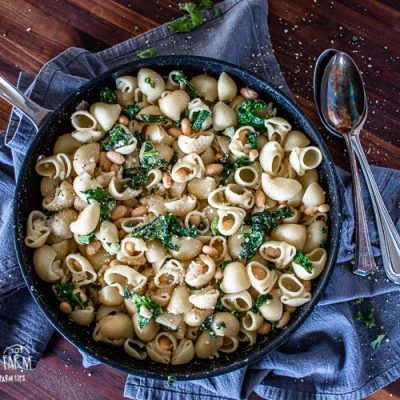 White bean and kale pasta in a frying pan on a grey towel, vertical.