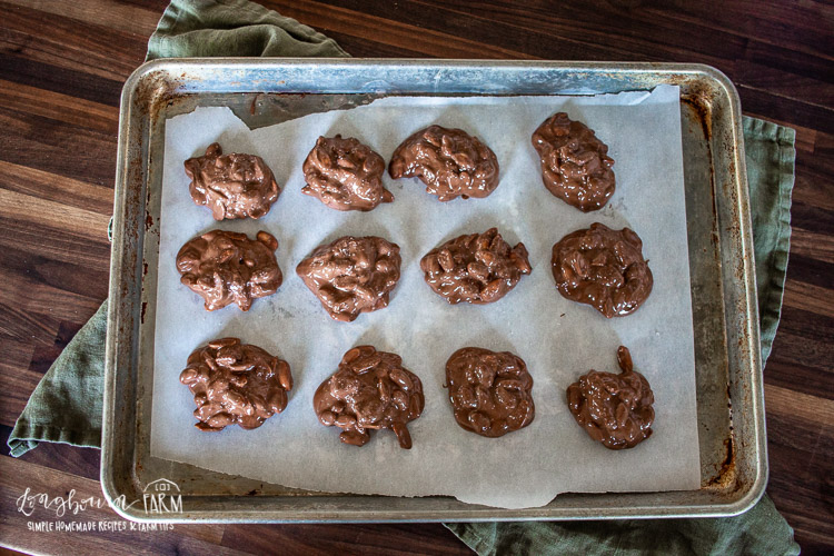 melted chocolate covered peanut clutters on a parchment-lined baking sheet