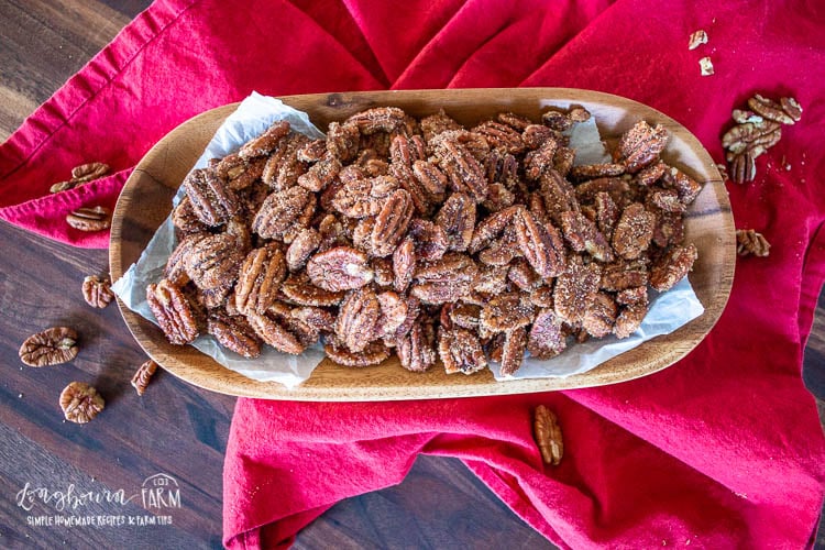 Rum spiced pecans in a wooden dish on a red towel, horizontal.