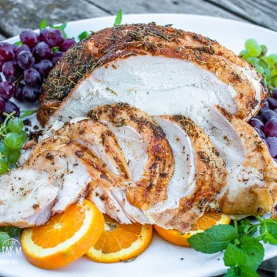 coin sliced smoked and seasoned turkey breast on a serving platter with grape bunches and sliced oranges