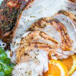 close-up coin sliced smoked and seasoned turkey breast on a serving platter with grape bunches and sliced oranges