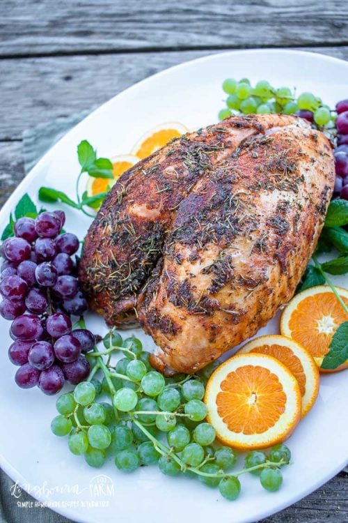 fully smoked and seasoned turkey breast on a serving platter with grape bunches and sliced oranges