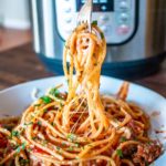 forkful of spaghetti over a bowl of spaghetti in front of the instant pot