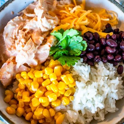 an upclose view of the mexican chicken in a bowl with cheese, corn, black beans, and white rice and garnish