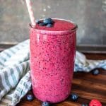 looking at a tall glass of berry smoothie from the side with scattered fresh berries