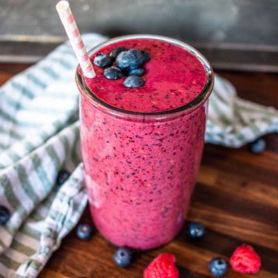 atall glass ofberrie smoothie with scattered berries and a kitchen towel