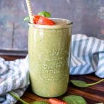 a delicious green smoothie with strawberry slices and spinach leaves scattered