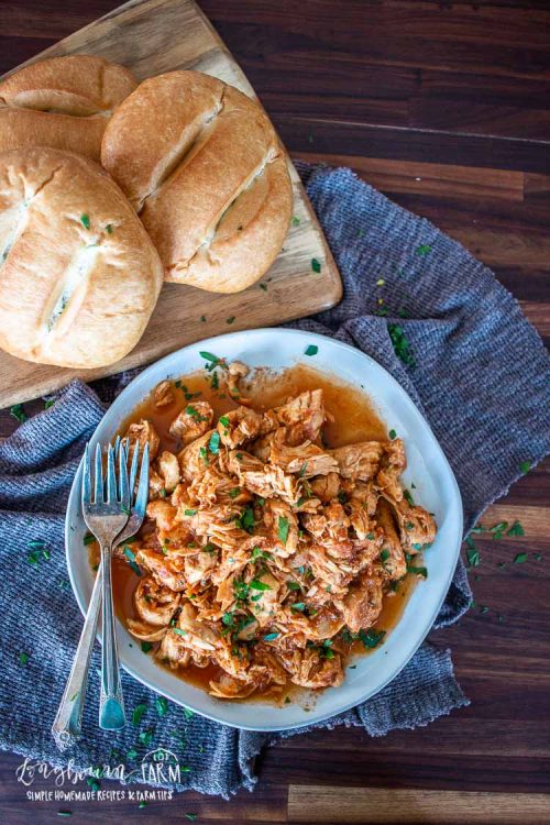 a bown full of instant pot bbq chicken with fresh bread rolls off to the side