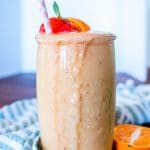 a tall glass of mango smoothie garnished with strawberry and oranges