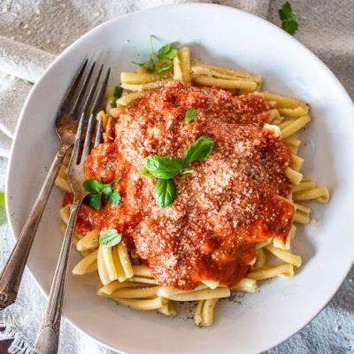a plate full of pasta with marinara sauce cheese and garnishes and two forks