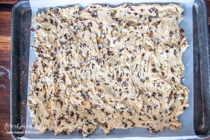 chocolate chip cookie bar batter on a parchment ined baking sheet