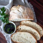 sliced ciabatta bread on cloth next to bowl of dip and fresh herbs