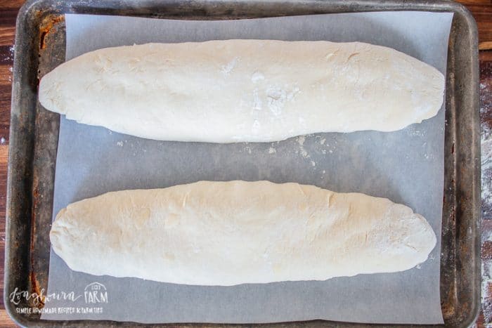 two raw loaves of french bread on a parchment lined baking sheet