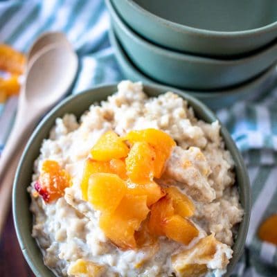 peaches and cream oatmeal in a bowl topped with fresh pieces and empty bowls to the side