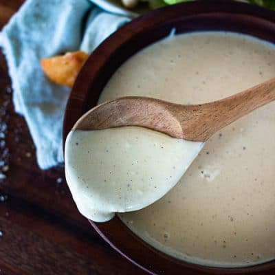 a wooden spoon in a bowl of caesar salad dressing