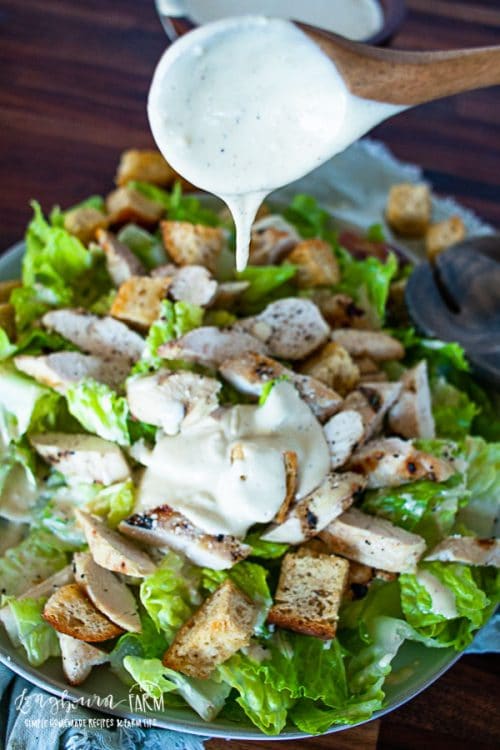 pouring caesar salad dressing off a wooden spoon onto a green salad