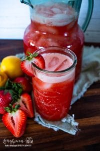 a glass of strawberry lemonade next to a pitcher and fresh fruit