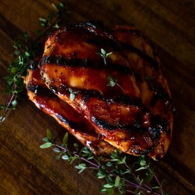 grilled bbq chicken on wooden board with fresh herbs