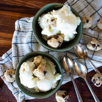 two bowls filled with cookie dough ice cream and scattered cookie dough balls and spoons around it
