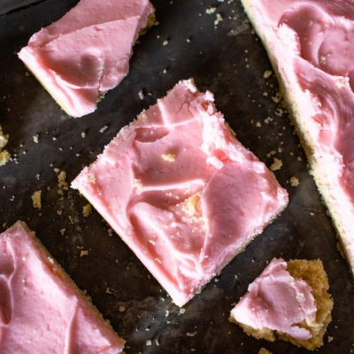 sliced and crumbled pink frosted sugar cookie bars on a baking sheet