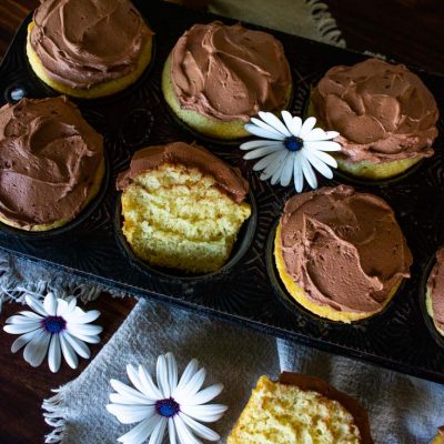 yellow cupcakes with chocolate frosting and garnished with fresh flowers