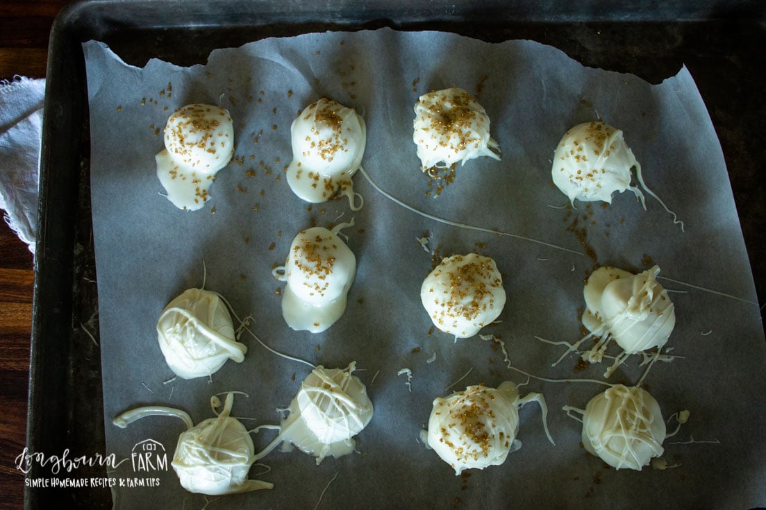 white chocolate dipped oreo truffles with golden sprinkles on a parchment lined baking sheet