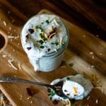 a jar full of loaded ranch dressing with a messy spoon and ingredients scattered around