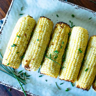 a large tray filled with green chive topped grilled corn on the cob