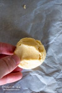 hand holding a snickerdoodle cookie dough ball above parchment paper