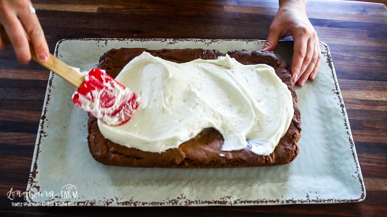 spreading cream cheese frosting over a gingnerbread cookie bar with a red rubber spatula