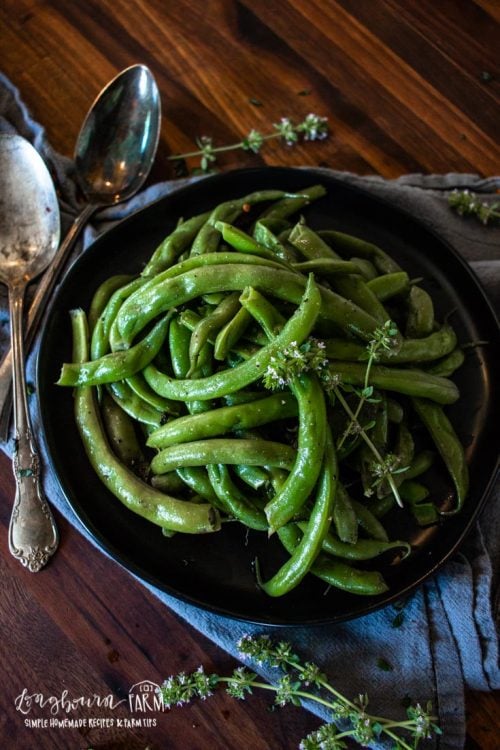 a bowl of green beans with fresh herbs next to two spoons