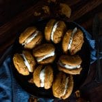 a dark plate filled with pumpkin whoopie pies and cookie crumbs to the side