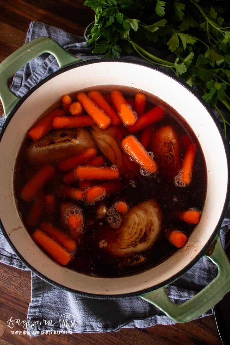 a dutch oven filled with broth liquid, onions, carrots, and more