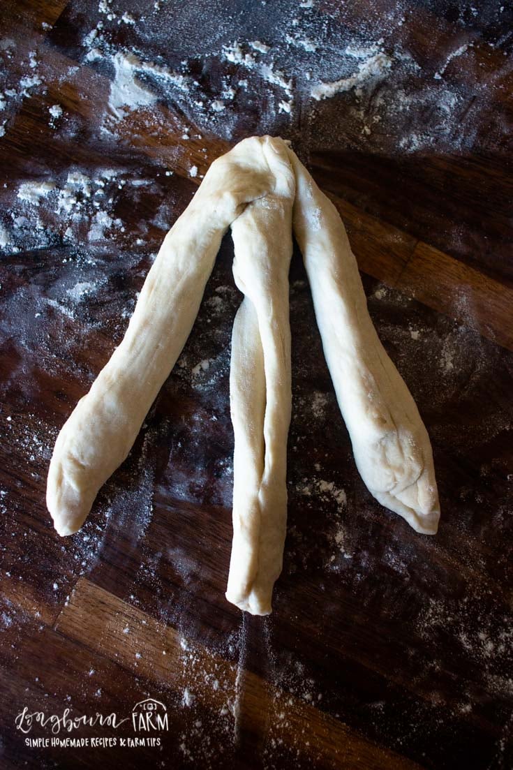three strands of bread dough dough on a floured surface