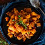 a dark plate topped with a pile of cooked butternut squash and fresh herb garnish
