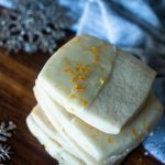 square shaped orange zest topped orange shortbread cookies next to snowflakes and a blue towel