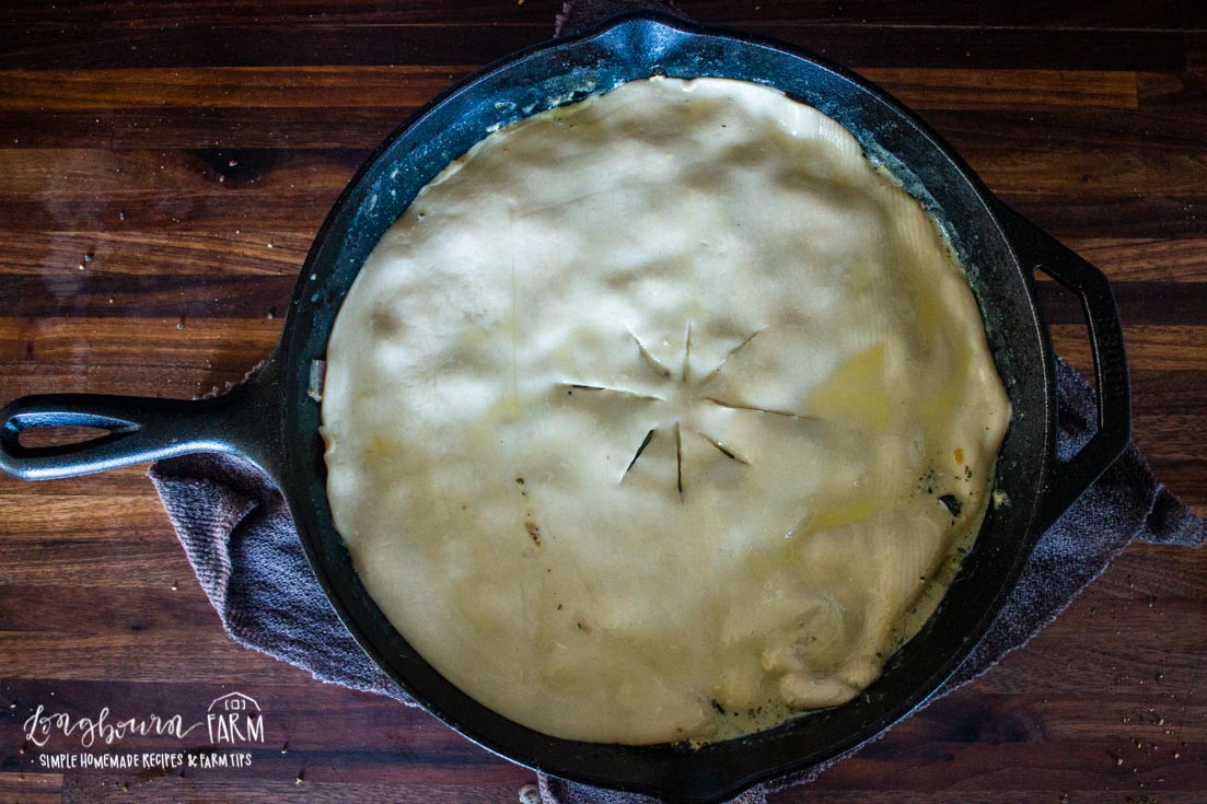 a raw pie crust on top of chicken pot pie filling in a skillet