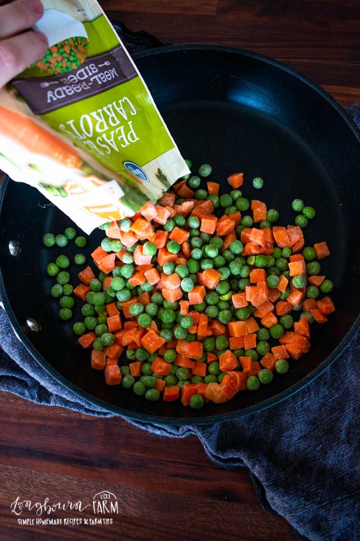 adding a bag of frozen peas and carrots to a skillet