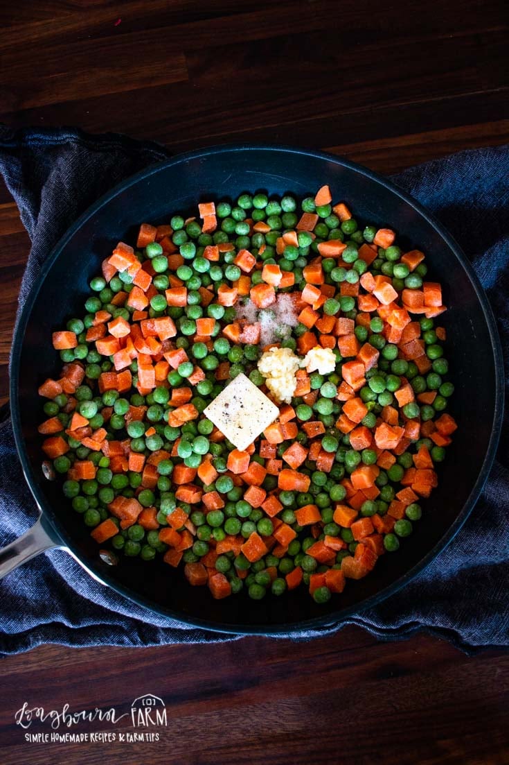 a skillet of frozen peas and carrots with butter and garlic and salt on top
