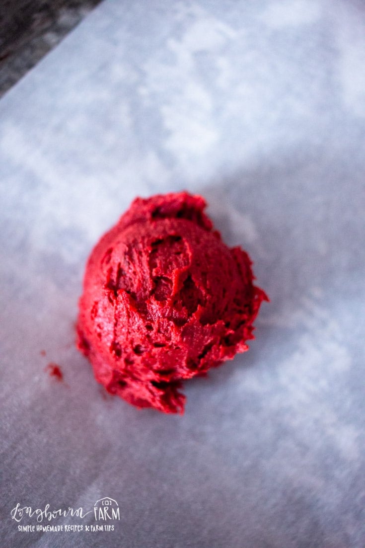 a scoop of red velvet cookie dough on a parchment lined baking sheet