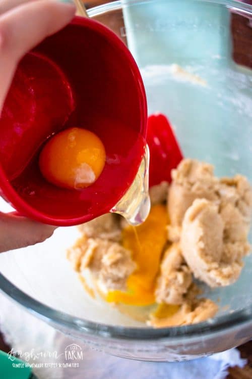 adding eggs to the glass bowl of dough