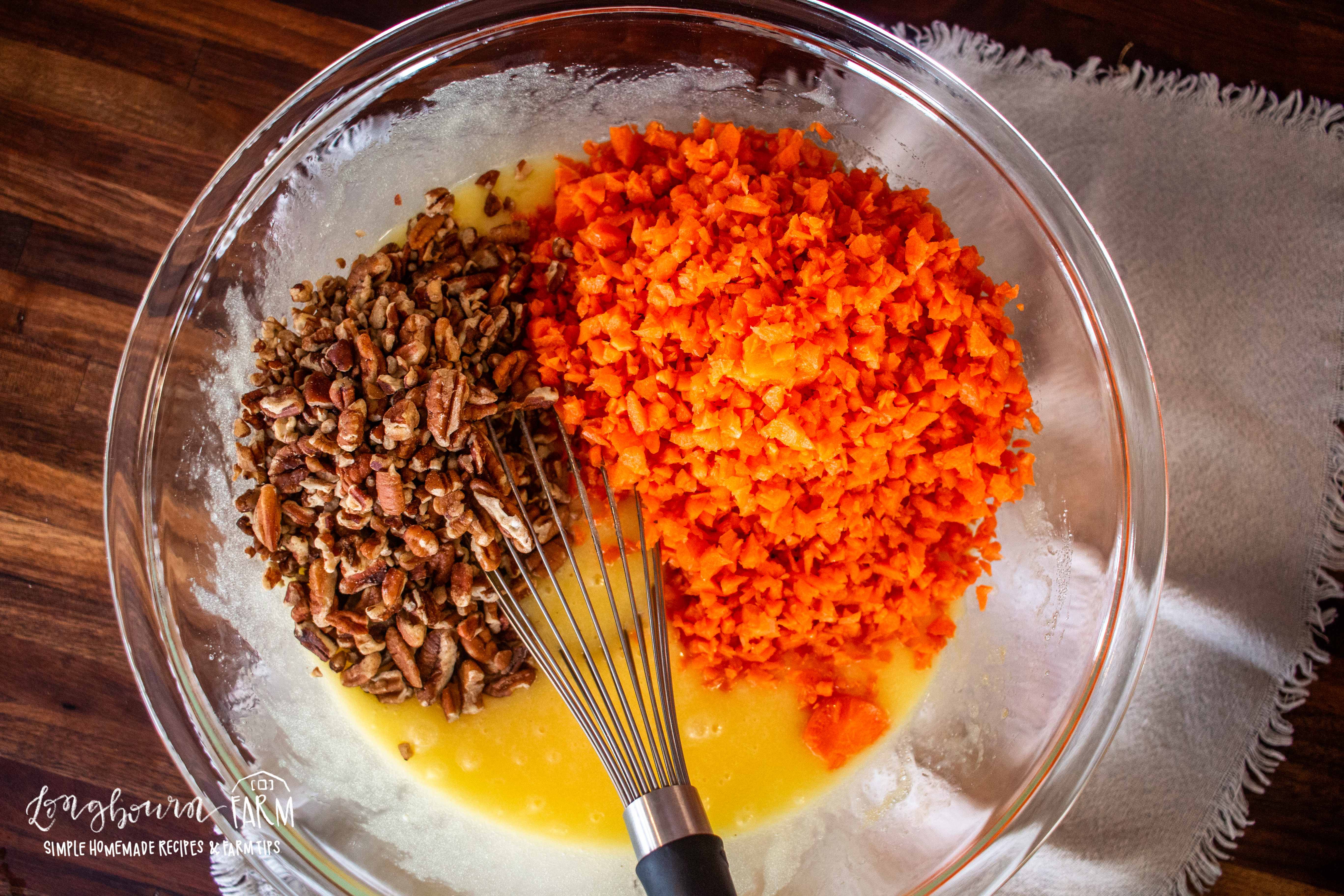 whisking grated carrot and walnuts into a bowl full whisked egg and sugar mixture for muffins