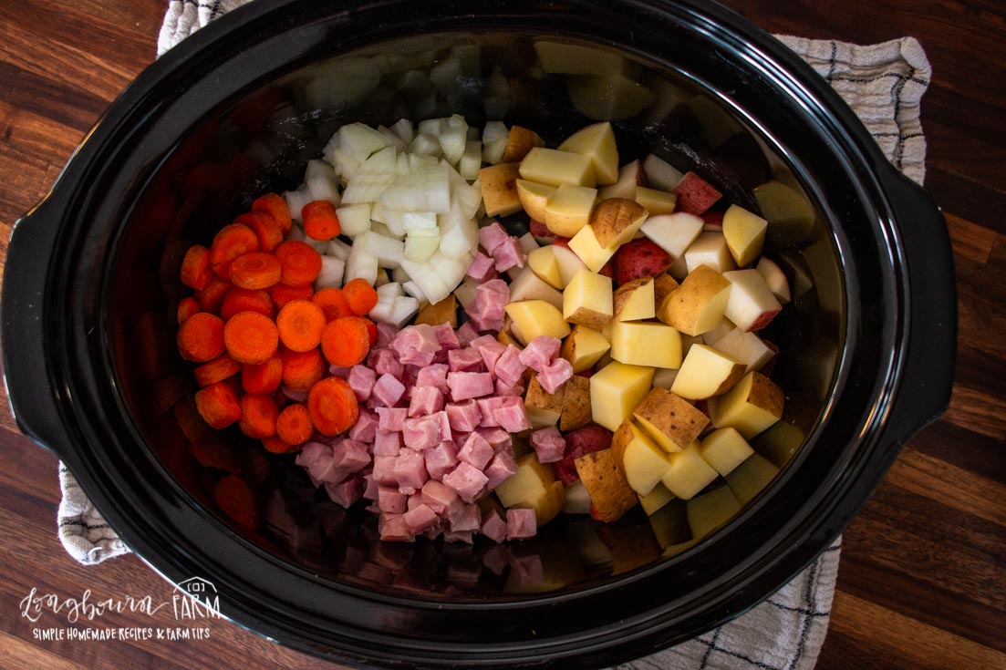 a crockpot full of carrot, onion, ham and potatoes